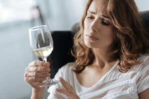A woman holds a glass of white wine wondering if she needs alcohol abuse counseling