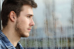 A man looks out a rainy window thankful for the trauma informed approach to his addiction treatment