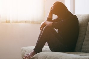 A woman sits on the couch thinking about her need for a depression treatment program
